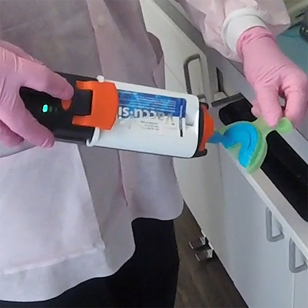 Dentist filling a dental tray with VPS impression material using the hand-held Vacu-Mixer. The machine is light enough that you can hold it in one hand, the tray in the other, and fill the tray in less than 10 seconds.